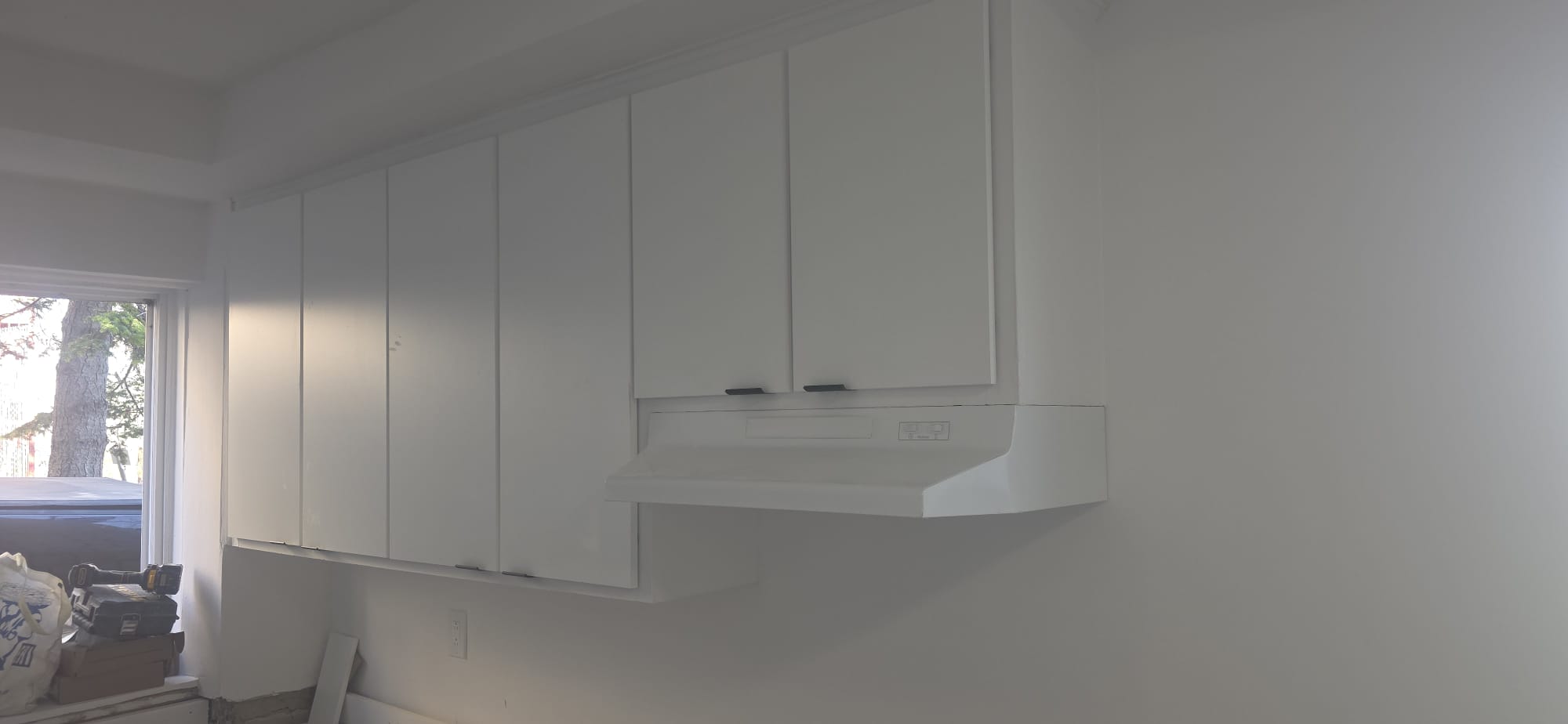 Armoires hautes et hotte neuve posées sur un mur de cuisine fraîchement fini.